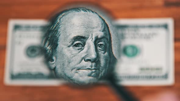 One Hundred Dollars Look Under Magnifying Glass on Wooden Table