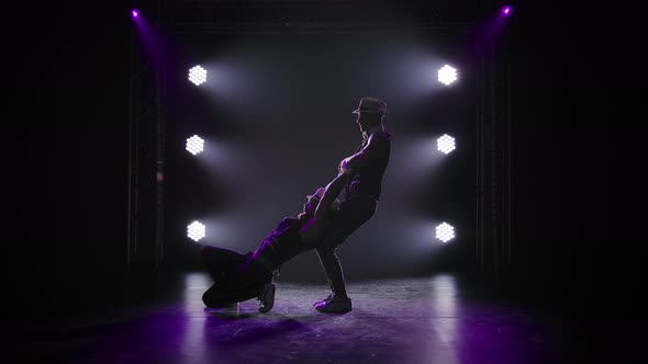 Group of Male Gymnasts Perform Acrobatic Stunts on Balancing. Silhouettes of Two Men on a Black