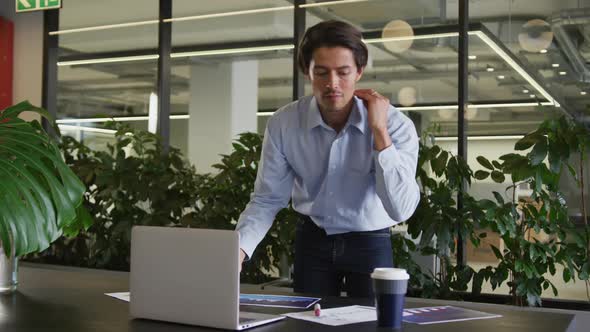 Caucasian businessman standing using laptop going through paperwork in modern office