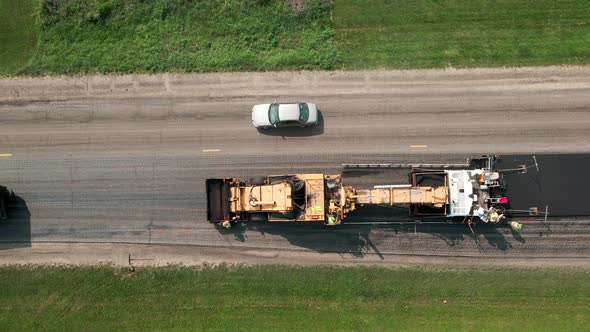 Birds eye view of asphalt paver laying blacktop and dump truck backing up to refill loose aggregate