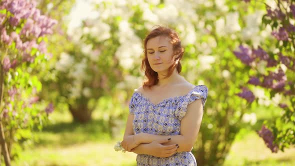 Romantic Young Woman Stands in Lilac Field and Holds White Flower Thinking About Love