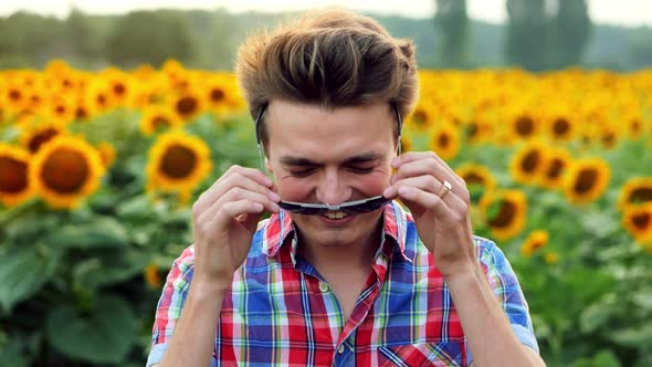 Cool and Stylish Modern Male Farmer Puts on Glasses Against the Background of a Field of Sunflowers