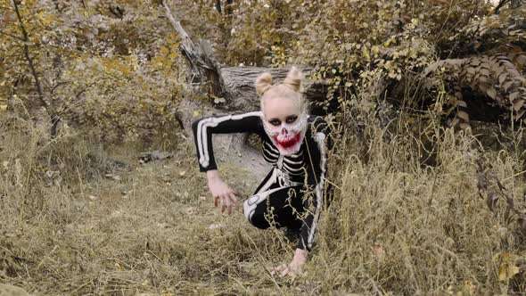 A girl with a scary make-up in a skeleton costume, a mask with rhinestones in a gloomy autumn forest