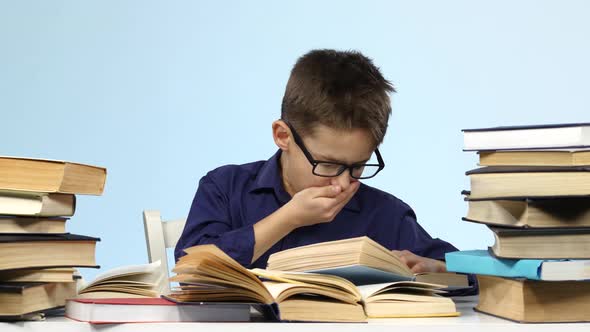 Boy Sits at the Table and Wearily Leafing Through a Book. Blue Background