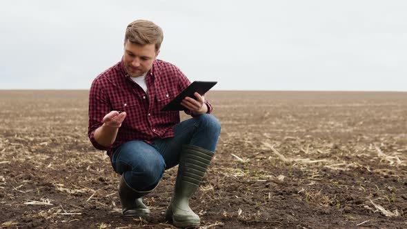 Farmer on a Field with a Tablet Before Planting Agricultural Cultures Studies the Condition of the