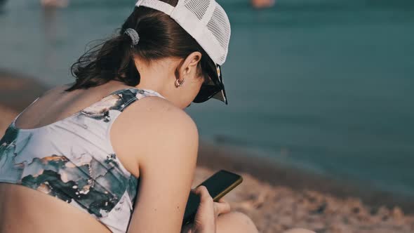 Young Woman Uses a Smartphone on the Beach