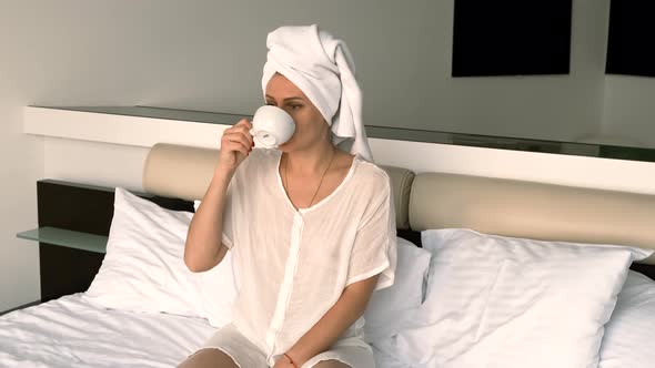 Girl Wearing Bathrobe and Towel Drinks Coffee While Sitting on the Bed