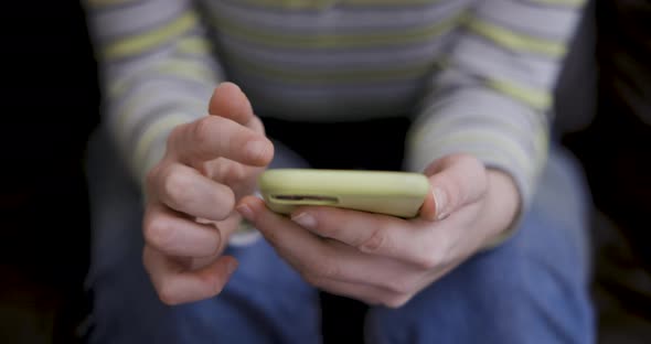 Close up shot of woman hands using a smart phone while sitting on the sofa at