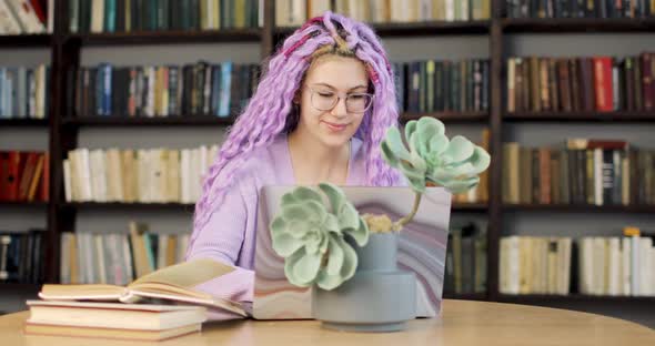 Young Woman with Long Colored Hair is Sitting at a Desk with a Laptop Working in the Library