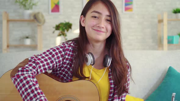 Beautiful Asian Girl with a Guitar in the Living Room of the Houselooking at the Camera Smiling