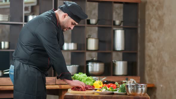 Focused Male Chef in Uniform Cutting Fresh Meat on Table at Kitchen
