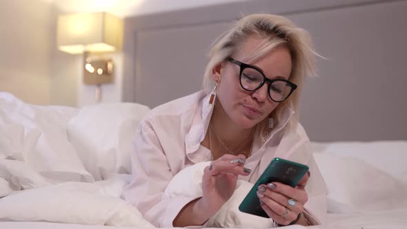 Sexy Blonde Lady is Using Smartphone in Bed Before Sleep Chatting and Sending Message