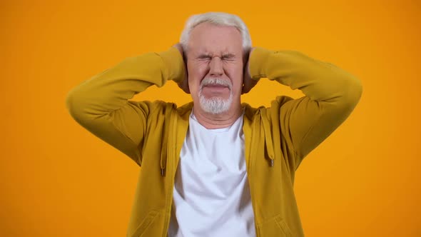 Retired Male Covering Ears by Palms Displeased With Gossips on Orange Background