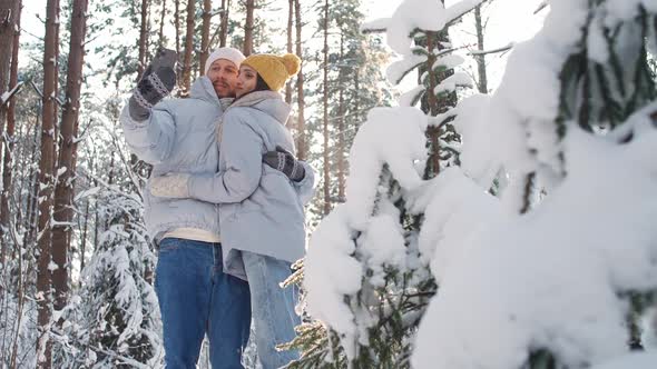 Young Couple Walks in a Winter Forest Man and Female Take a Selfie on a Smartphone