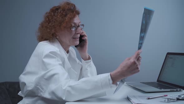 Elderly Caucasian Woman Doctor Analyze Xray Image and Talk with Mobile Phone About Diagnostics in
