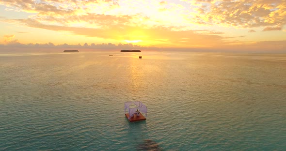 Aerial drone view of a man and woman having dinner on a floating raft boat at sunset