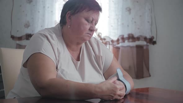 Mature Obese Women Measuring Pressure with Digital Sphygmomanometer While Sitting at Table. Senior