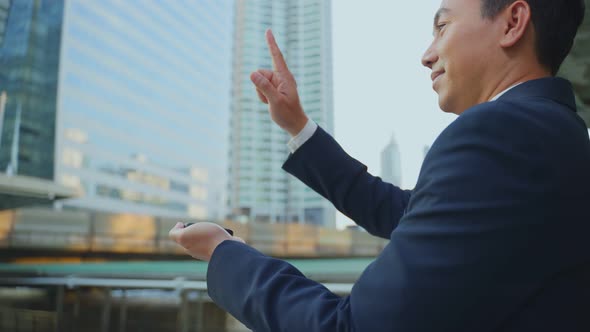 Asian business man standing outdoor in city holding mobile phone and finger scrolls across screen.