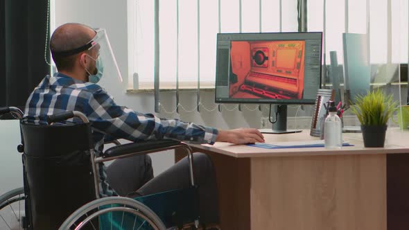 Handicapped Game Developer in Wheelchair with Mask Working