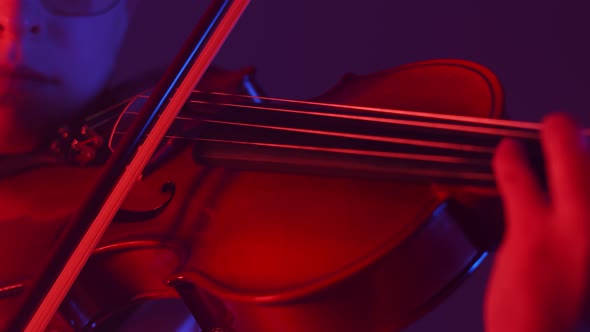 Artist Woman Engaged in Playing Violin in the Red Light of the Studio