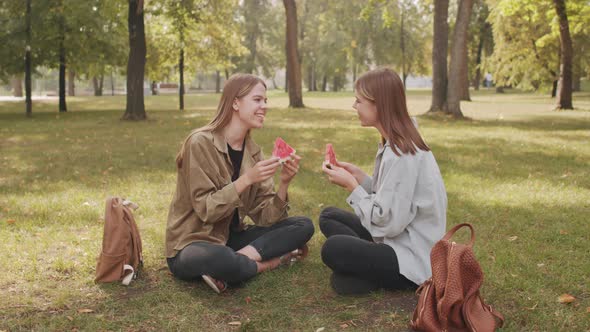 Happy Twin Sisters Eating Watermelon in Park