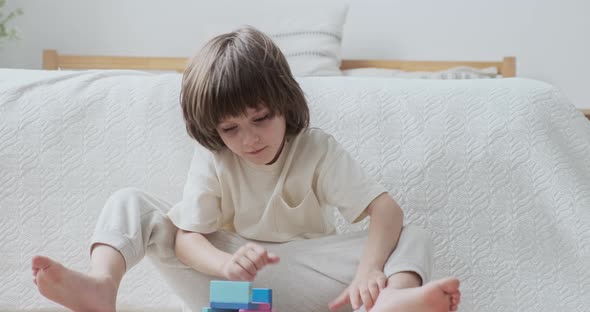 Confident Male Kid Building Multicolored Wooden Blocks Sitting on Floor at Home