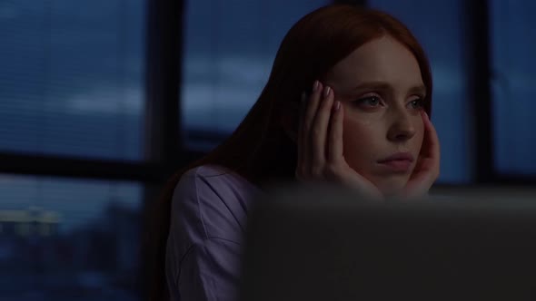 Closeup Face of Tired Sad Woman Sitting at Desk with Laptop in Dark Office Room Near Window at Night