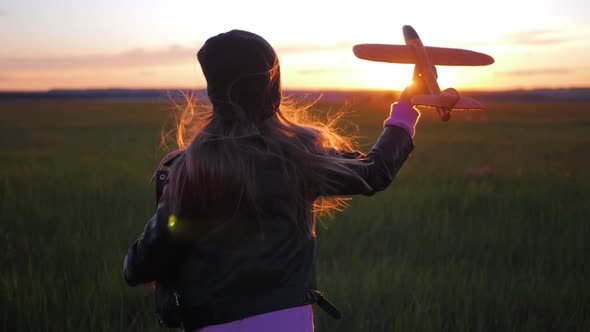 Happy Little Girl Child Runs at Sunset on the Meadow with a Toy Plane