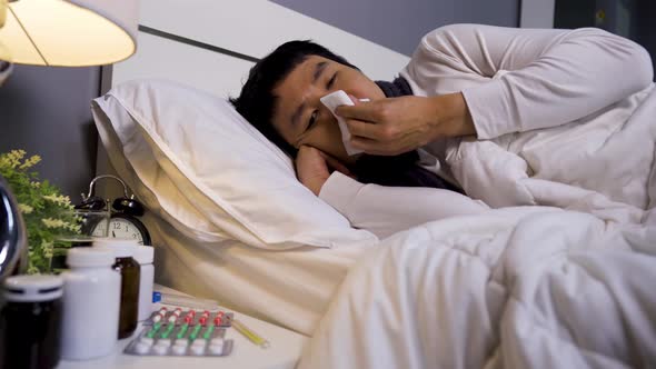 sick man sneezing into tissue lying in bed