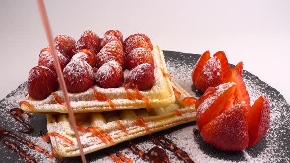 Belgian waffles with strawberry, sweet strawberry topping and powdered sugar on a stone board 