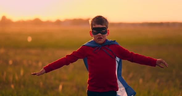 Boy in Superhero Costume and Mask Running Across the Field at Sunset Dreaming and Fantasizing