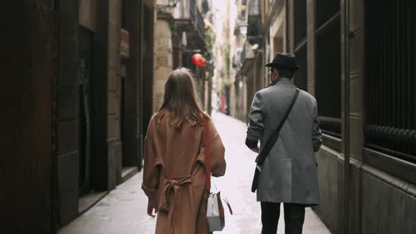 Back View of Young Stylish Attractive Friends Walking Through Tight Street
