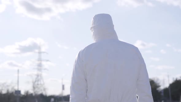 Back View of Young Man in White Protective Suit Walking Along Half-empty Road on Sunny Day. Urban