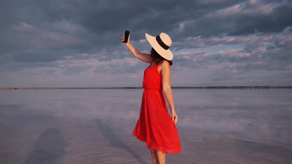Young Woman Takes a Selfie in a Beautiful Unusual Place. Girl in a Red Dress, Hat and Sunglasses 