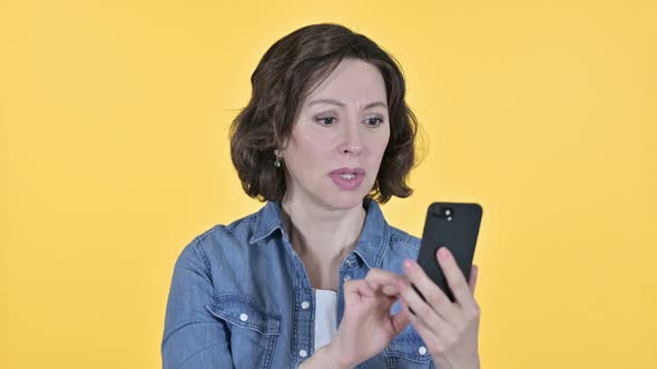 Old Woman with Loss on Smartphone, Yellow Background 