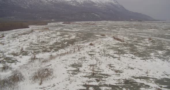 Aerial helicopter wide shot, tilt up past Alaskan mountain range, over valley to showcase snowy slop