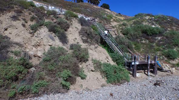 Aerial shot of a young man running stairs on the side of a cliff by the ocean