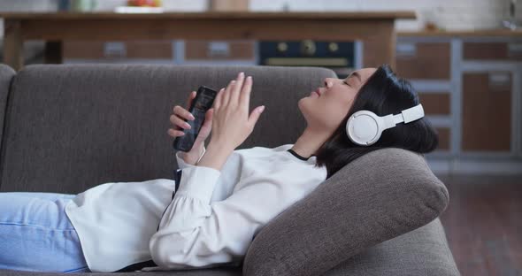 Happy Student Attractive Asian Girl is Listening to Music in Headphones Holding Smartphone Touching