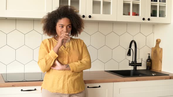 Attractive African Woman is Drinking Water From Glass Standing in the Kitchen