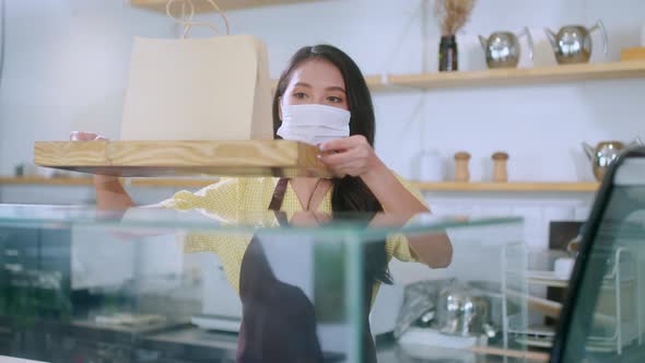 Attractive asian female cafe worker wears face mask and gloves giving takeaway food bag