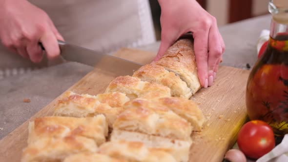 Woman Slicing Baguette on Wooden Cutting Board at Domestic Kitchen