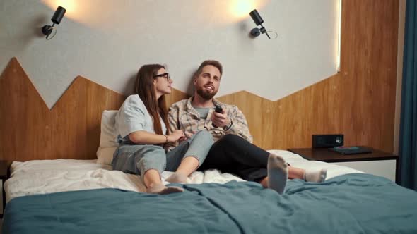 young couple watching TV in hotel room and guy is not happy