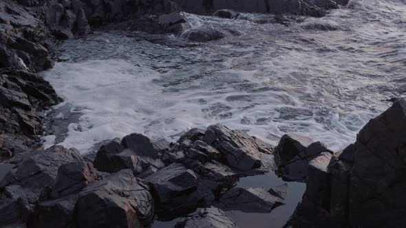 Calm ocean waves rolling into rocky coast line at sunset. Tripod slow motion shot in 4K.