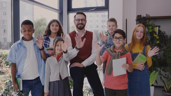 Male Teacher with Middle School Children Looking at Camera and Waving Hands