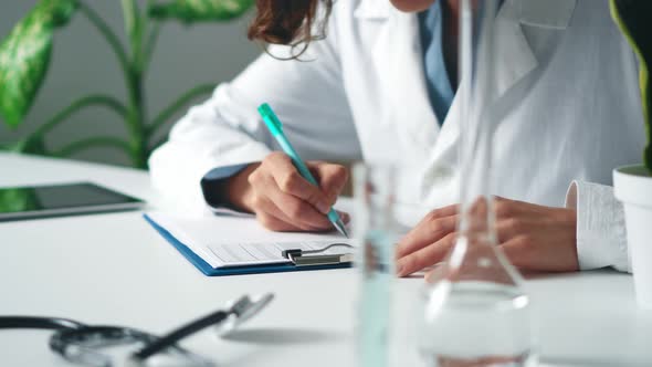 Young Female Doctor In Office Writes Medical Documentation, Uses A Tablet. Filling Out Medical Form