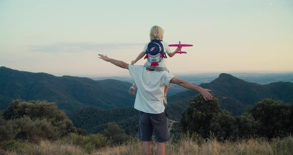 Child Boy Sit on Fathers Neck and Play with Toy Aeroplane on Travel to Mountain