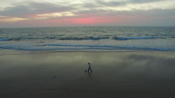 Aerial shot of little boy playing soccer on the beach at sunset.