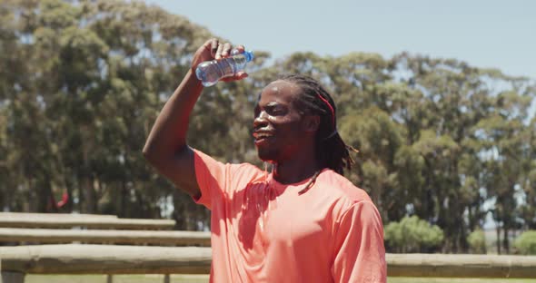 Fit african american man with dreadlocks pouring water over head after exercising in the sun