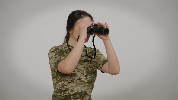 Young Female Soldier with Binoculars Looking Away Posing at Grey Background