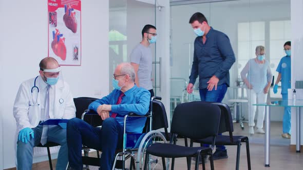 Invalid Old Man with Face Mask Discussing with Doctor in Hospital Waiting Area